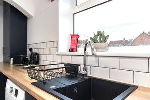 Eine Küche mit einem schwarzen Spülbecken, einem Fenster mit einem Kaktus und einer roten Feuerschutzdecke am Fensterbrett.