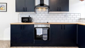 Een moderne keuken met donkere kastjes, een magnetron, een oven en een betegelde achterwand.
