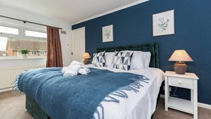 Een slaapkamer met een bed, twee nachtkastjes, een raam met gordijnen en twee ingelijste foto’s aan de muur.