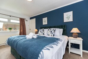 Ein Schlafzimmer mit einem Bett, zwei Nachttischen, einem Fenster mit Vorhängen und zwei gerahmten Bildern an der Wand.