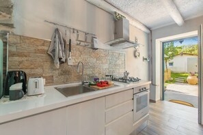 A modern kitchen with a stone backsplash, stainless steel appliances, and a view of the outdoor garden. - Dimora Della Rocca Private Garden, Wifi, BBQ & Parking (Angera)