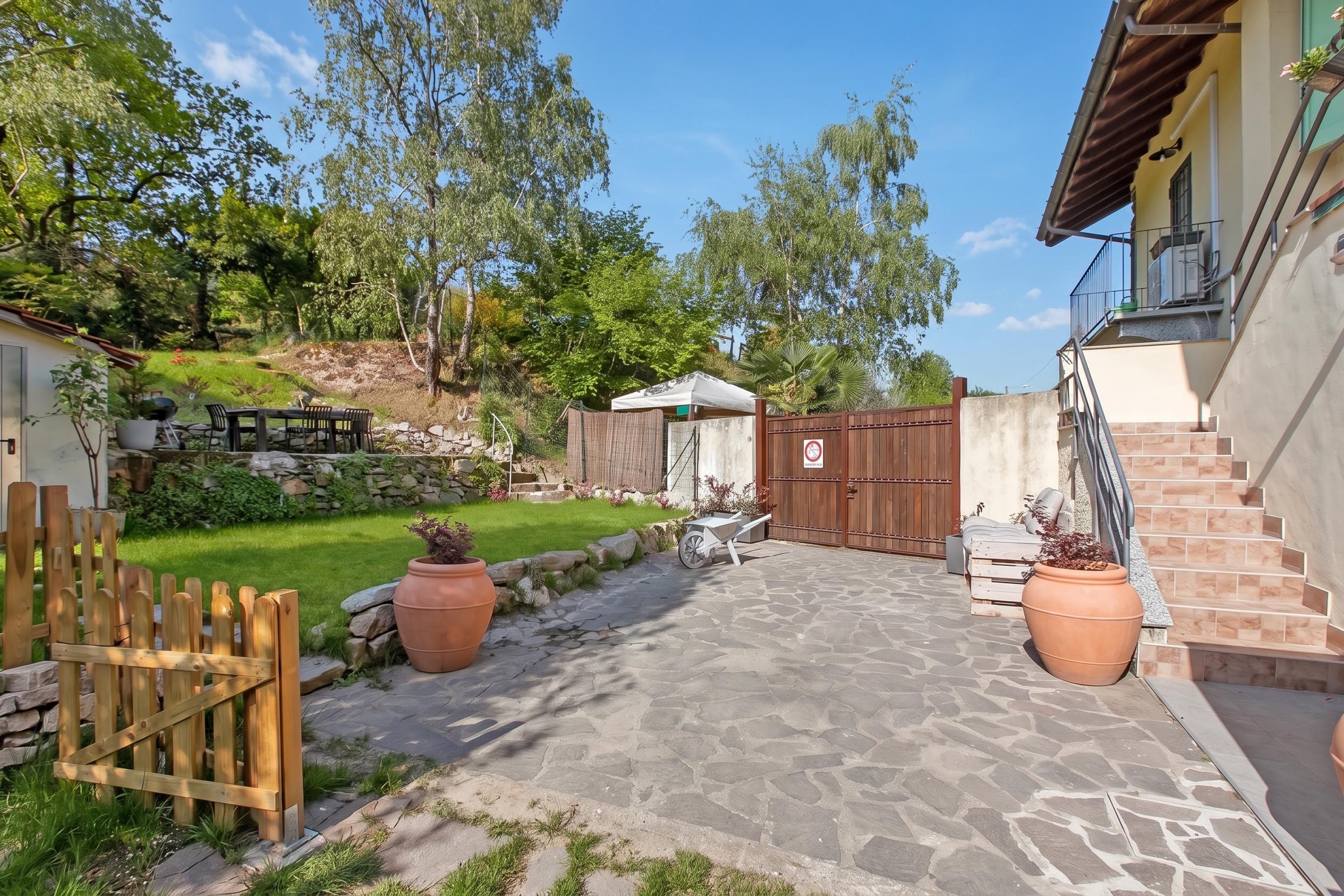 Un patio lastricato con recinzione in legno, piante in vaso e ingresso con cancello.