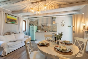 A modern kitchen with a stone backsplash, a dining table set for two, and a white sofa in the living area. - Dimora Della Rocca Private Garden, Wifi, BBQ & Parking (Angera)