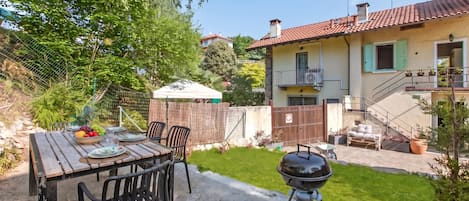 A patio with a table set for dining, a barbecue grill, and a house with a balcony in the background.