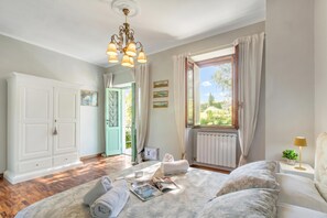 A bedroom with a bed, a window with curtains, a radiator, and a chandelier. - Dimora Della Rocca Private Garden, Wifi, BBQ & Parking (Angera)