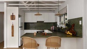 A kitchen with white cabinets, a green island, two wicker chairs, and pendant lights. - Wondervale - Escape to the Southern Highlands (Burrawang)