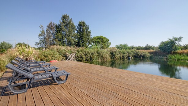 Una terraza de madera con sillones de descanso y una masa de agua tranquila al fondo.