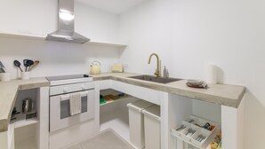 Una cocina moderna con armarios blancos, una campana extractora de acero inoxidable, un lavamanos integrado y una encimera con una tetera y un tostador.