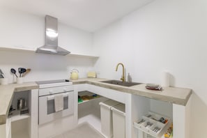 Una cocina moderna con armarios blancos, una campana extractora de acero inoxidable, un lavamanos integrado y una encimera con una tetera y un tostador.
