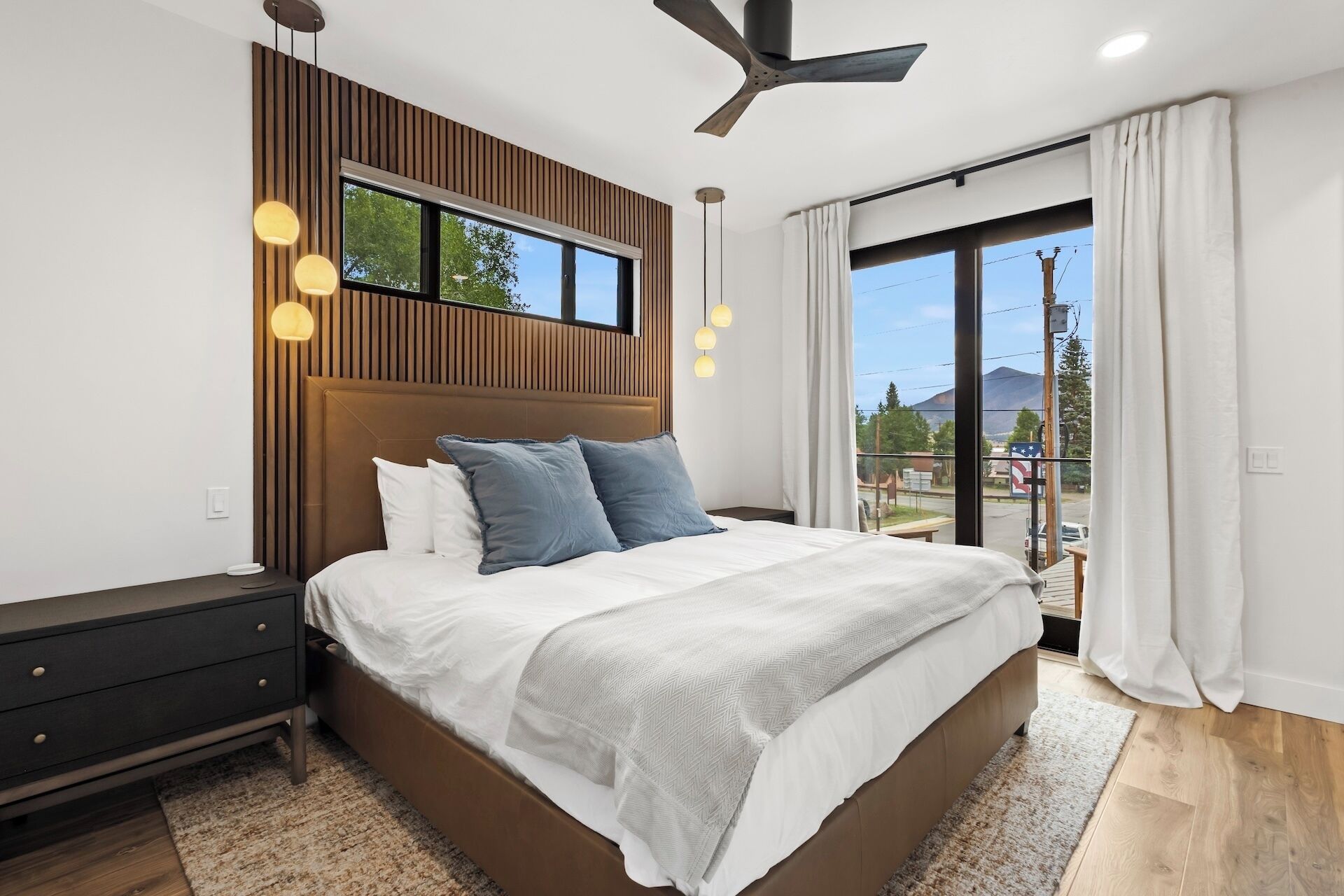 A modern bedroom with a large bed, a wooden accent wall, and a view of the outdoors.