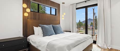 A modern bedroom with a large bed, a wooden accent wall, and a view of the outdoors.