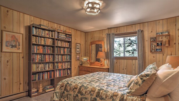 A bedroom with a large bookshelf, a bed with patterned bedding, a dresser, and a window with curtains. - New Listing! Quiet Mtn Cabin | River and Mtn Views | Expansive Deck (Creede)