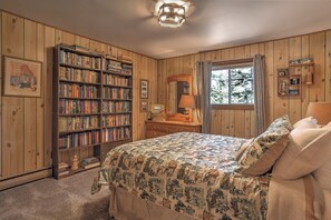 Quarto com uma grande estante de livros, uma cama com roupa de cama estampada, cômoda e janela com cortinas.