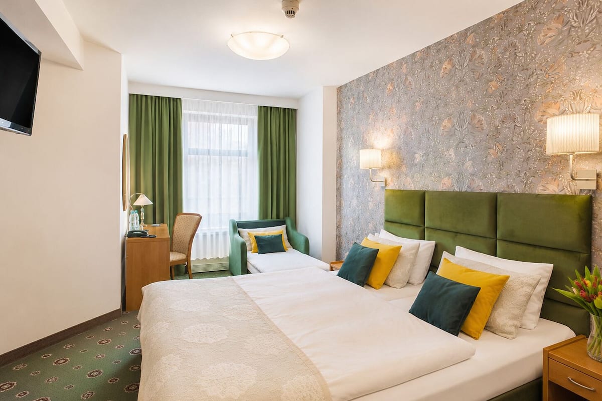 A hotel room with a large bed, a desk with a chair, a television, and a window with curtains.