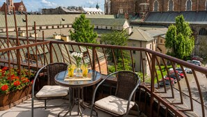 A terrace with wicker chairs and a table, overlooking a historic building with a red roof. - Hotel Secesja (Kraków)