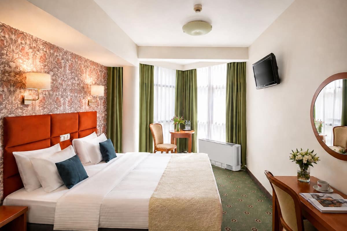 A hotel room with a bed, a desk, a chair, a television, and a window with curtains.