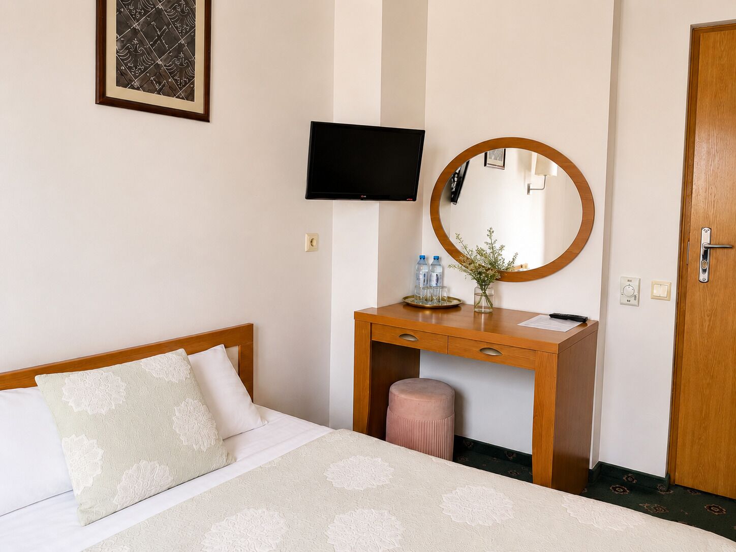 Une chambre d’hôtel avec un lit, un bureau en bois avec un miroir, une télévision et une porte.