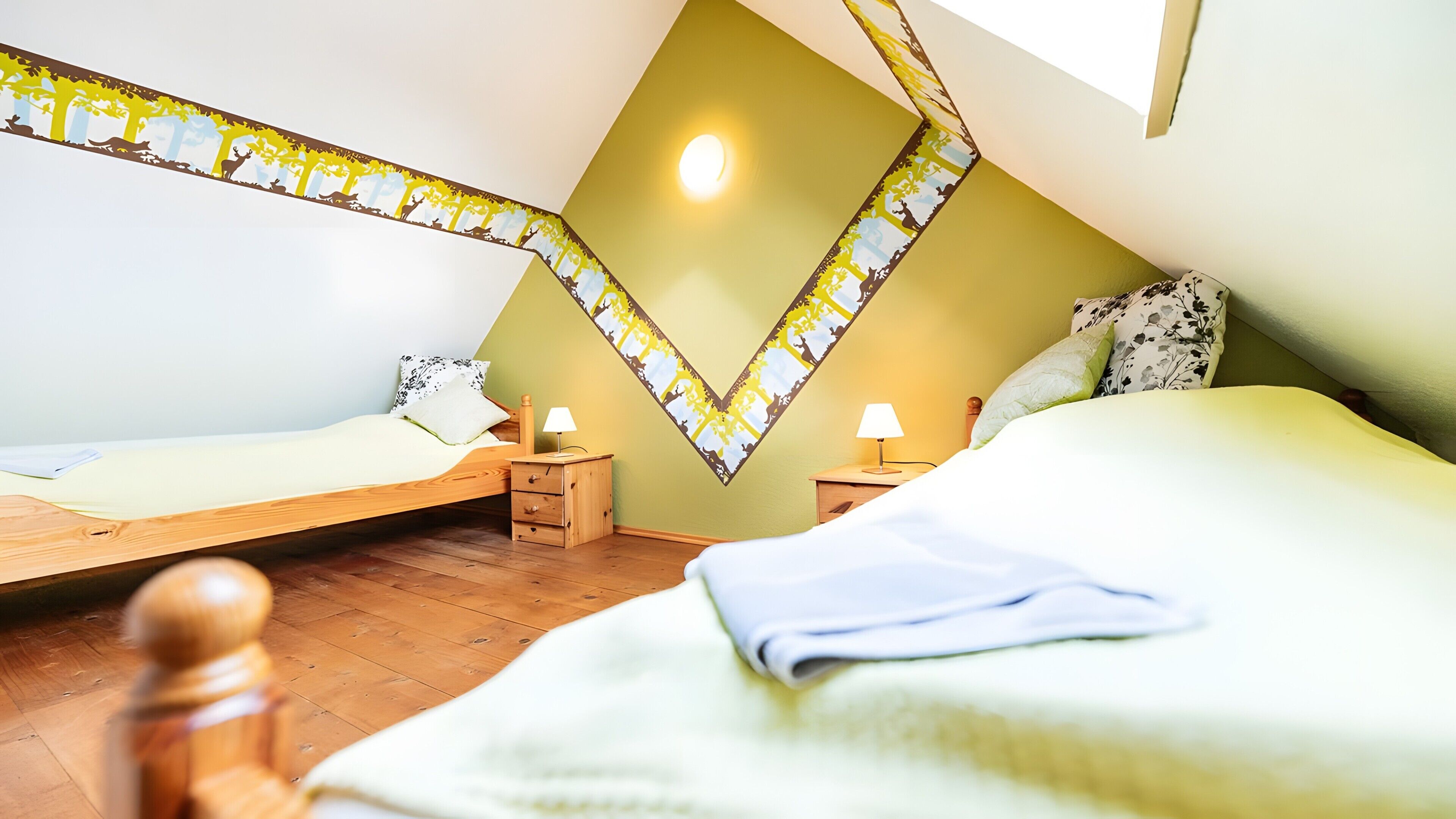 A bedroom with two beds, a wooden floor, and a green accent wall.