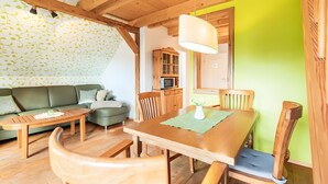 A cozy living room with a wooden dining table, green sofa, and wooden chairs. - Holiday Apartment for 4 Guests (60 m²) on Fehmarn (Fehmarn)