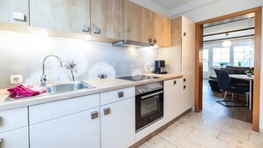 Una cocina moderna con un lavamanos de acero inoxidable, armarios de madera, horno empotrado y un comedor con mesa y sillas.