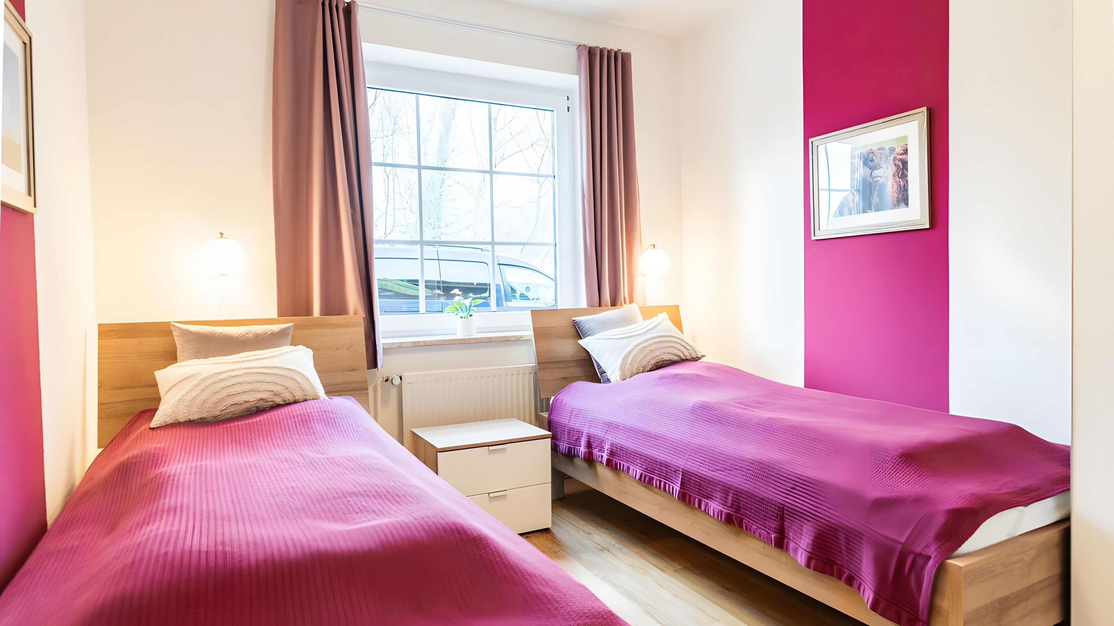A bedroom with two beds, a window with curtains, a radiator, and a framed picture on the wall.
