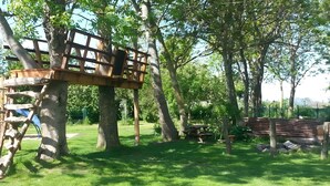 Una estructura tipo casa del árbol construida en un árbol grande, rodeada de hierba y otros árboles.