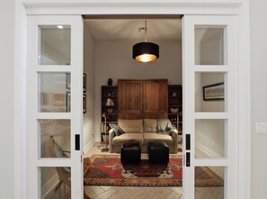 Ein Zimmer mit einer Couch, Poufs, einem Teppich, einem Schrank und einer Pendelleuchte.