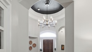 A hallway with a herringbone wooden floor, a black leather rug, a chandelier, and a door at the end. - Luxury in Desert Ridge (Phoenix)