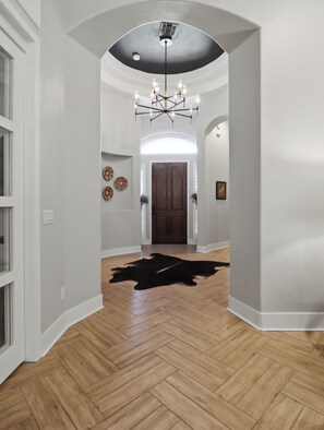 Ein Flur mit Fischgrätparkett, einem schwarzen Lederteppich, einer Chandelierleuchtre und einer Tür am Ende.