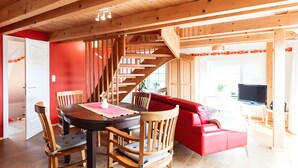 Un interior de madera con una mesa de comedor, sillas, un sofá rojo y una escalera.