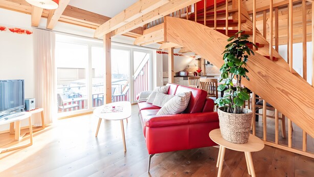 Una sala de estar moderna con un sofá rojo, una mesita blanca y una escalera de madera.