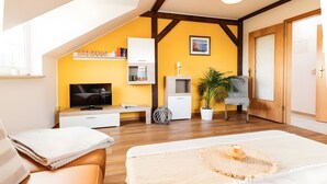Une chambre moderne équipée d’une télévision, d’un lit, d’une chaise, d’une plante et d’une étagère remplie de livres.