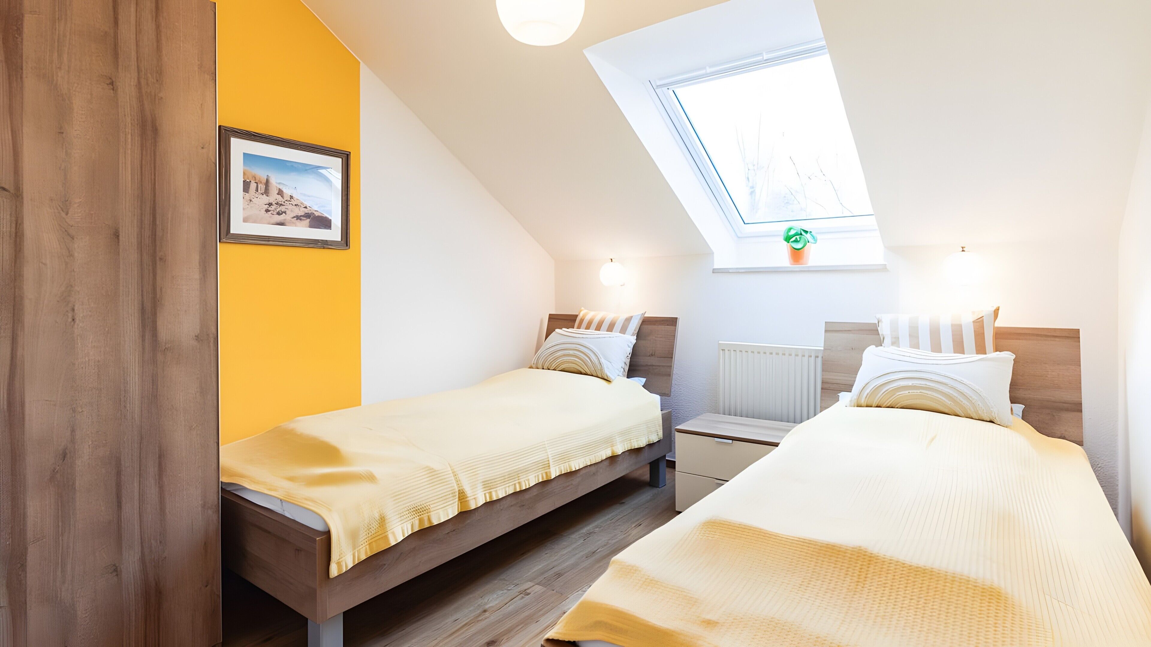 A bedroom with two beds, a skylight, a radiator, and a framed picture on the wall.