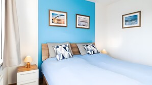 A double bed with a wooden headboard, two pillows, a bedside table with a lamp, and two framed pictures on the wall. - Holiday Apartment for 4 People (70 m²) in Fehmarn (Fehmarn)