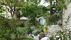 A garden with various plants and flowers, a white fence, and a small blue house. - Double Room with Bathroom and Balcony, Mountain View (Merano)