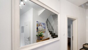 A hallway with a white-framed mirror reflecting a staircase, a door, and a wall-mounted plant with a heart-shaped decoration. - Double Room with Bathroom and Balcony, Mountain View (Merano)