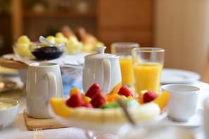 Una escena de desayuno con un plato de fruta, una jarra y un vaso de zumo de naranja.