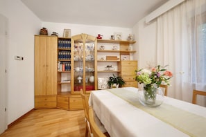 Ein Zimmer mit einem Holzschrank, einem Tisch mit weißem Tuch und Regalen mit verschiedenen Gegenständen.