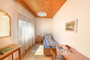 Ein kleiner, gemütlicher Raum mit Holzbalkendecke, einem Bett, einem Tisch und einem Stuhl.