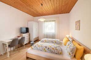 Un dormitorio con cama, escritorio, silla, televisor y ventana.