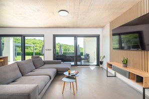 Ein modernes Wohnzimmer mit einem Ecksofa, einem Couchtisch, einem Flachbildfernseher und einer Glastür, die auf einen Balkon führt.