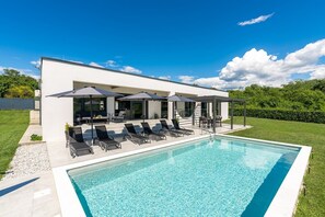 Ein moderner Poolbereich mit Liegestühlen, Sonnenschirmen und einem klaren, blauen Pool.