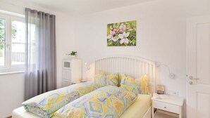 A bedroom with a bed, bedside tables, a window with curtains, a wall-mounted radiator, and a painting. - Villa Thaler Apartment with Mountain View and Rooftop Terrace (Merano)