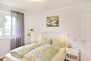 A bedroom with a bed, bedside tables, a window with curtains, a wall-mounted radiator, and a painting. - Villa Thaler Apartment with Mountain View and Rooftop Terrace (Merano)
