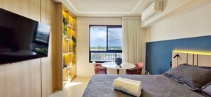 Ein modernes Hotelzimmer mit Bett, Fernseher, einem kleinen Tisch mit Stühlen, einem Balkon mit Aussicht und einem Bücherregal.