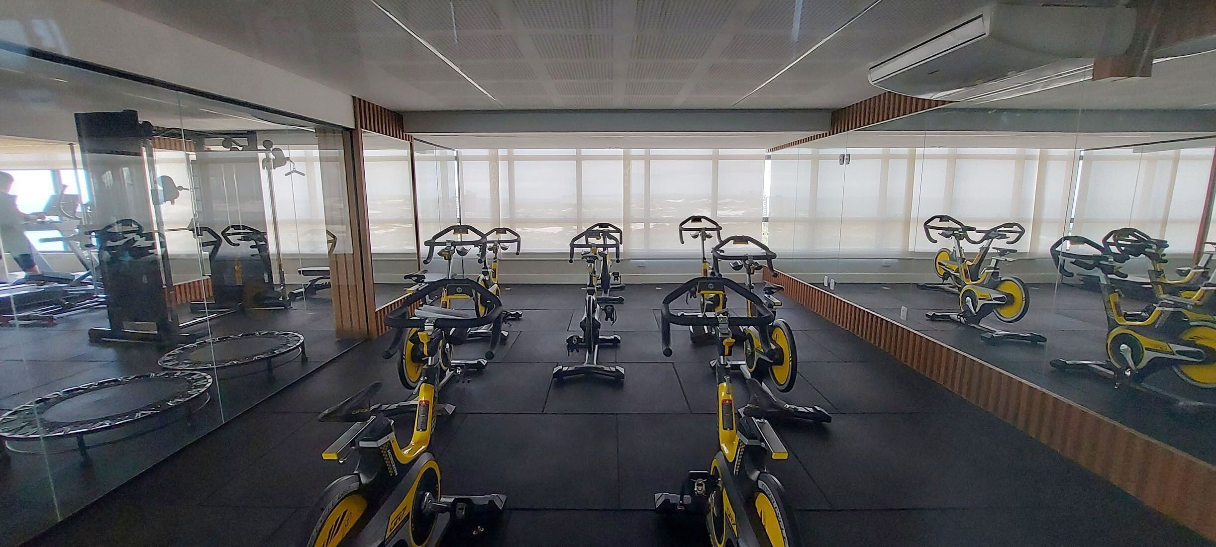 Un gimnasio con bicicletas estáticas y máquinas elípticas, ventanas amplias y espejos en las paredes.