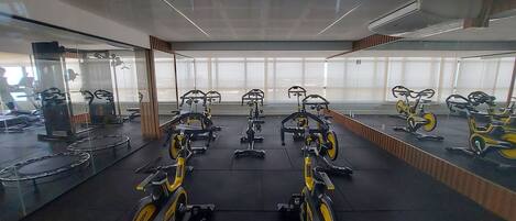 Un gimnasio con bicicletas estáticas y máquinas elípticas, ventanas amplias y espejos en las paredes.