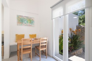A dining area with a wooden table and chairs, a bench with yellow cushions, and a colorful abstract painting on the wall.