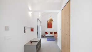 A hallway leading to a bedroom with a bed, a small table, and a wall-mounted shelf. - Wellness Garden Cottage with Yoga, Pilates and Natural Pond (Moncarapacho)
