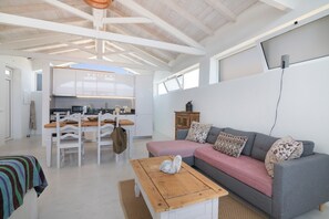 Una sala moderna con un sofá gris, una mesa de centro de madera y una zona de comedor blanca.